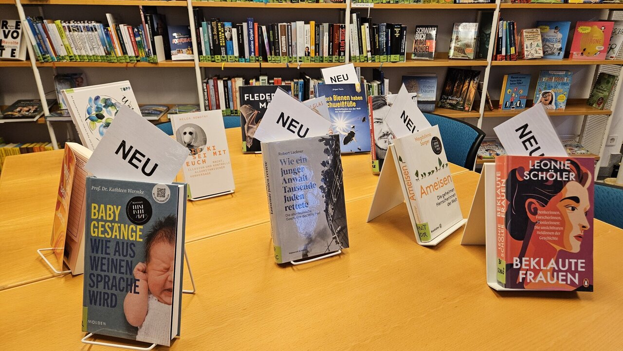 Auf einem Tisch sind Bücher aufgestellt mit einem Zettel auf dem Neu steht