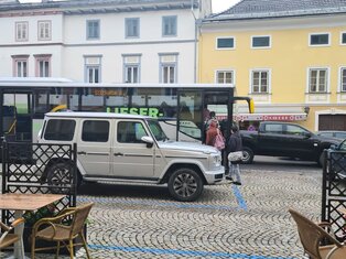 Ansicht vom Gasthof Alte Post Richtung Hauptplatz. Ein Bus steht auf der Bushaltestelle. Die Parkflächen rund herum sind alle voll. Die Flächen rund um die Bushaltestelle sind gering