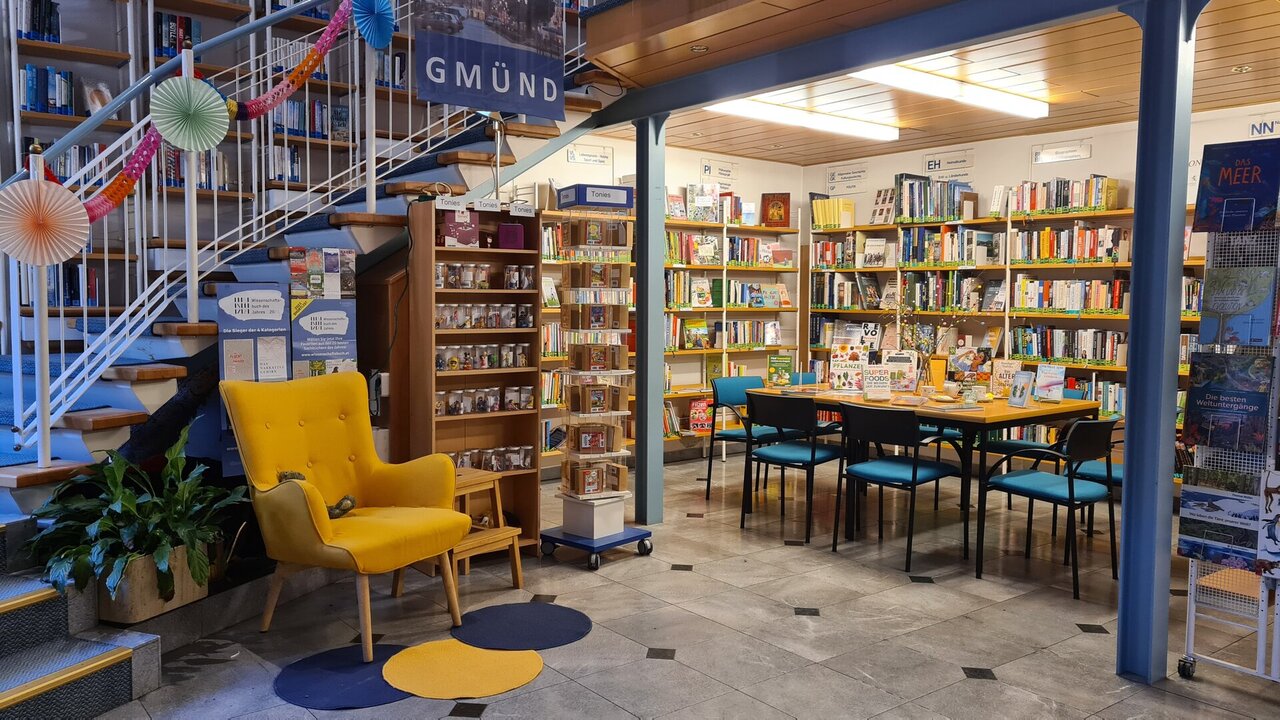 Ein großer Raum mit vielen Bücherregalen, in der Mitte steht ein gelber bequemer Lesesessel