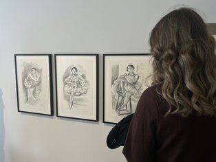 Eine Frau schaut sich drei Gemälde an einer Wand an