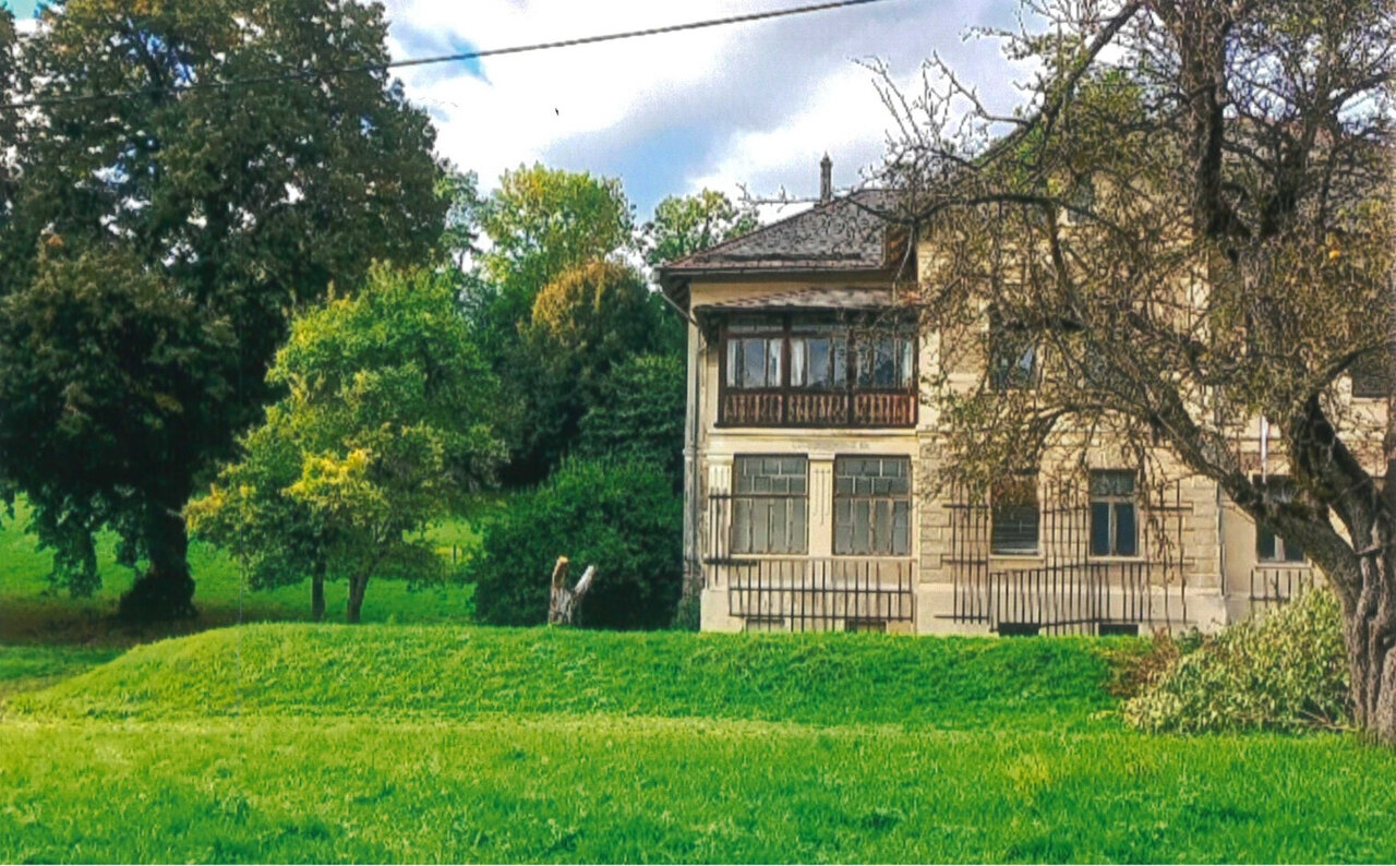 Eine alte Villa in einem großen, grünen Garten mit Bäumen und Sträuchern