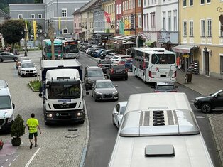 Blick vom Stadtturm Gmünd auf den Hauptplatz Gmünd. Durch das Untere Stadttor fährt ein Bus auf den Hauptplatz. Beide Bushaltestellen sind besetzt. Zwischen den Bussen fahren Autos und LKW.