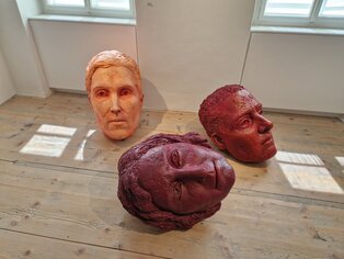 drei bunte Skulpturen in Form eines menschlichen Kopfes liegen und stehen am Boden
