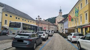 Blick vom Hauptplatz zum Stadtturm Gmünd. Alle Parkplätze sind belegt auf der Bushaltestelle parkt ein Bus der Firma Bacher Reisen